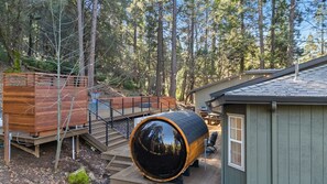 A cabin with a wooden deck, a large barrel, and a small shed.
