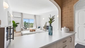 Una cocina moderna con armarios blancos, una isla central y vistas al exterior.
