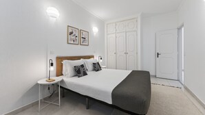 Un dormitorio con cama, mesitas de noche, armario y puerta.
