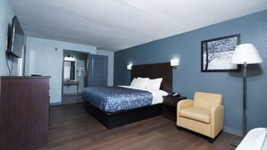 A hotel room with a bed, a chair, a desk, a mirror, and a picture on the wall. - Red Carpet Newnan (Newnan)