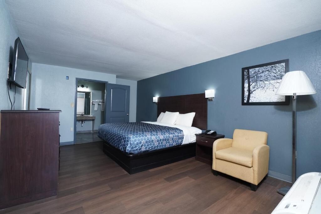A hotel room with a bed, a desk, a chair, a TV, and a painting on the wall.