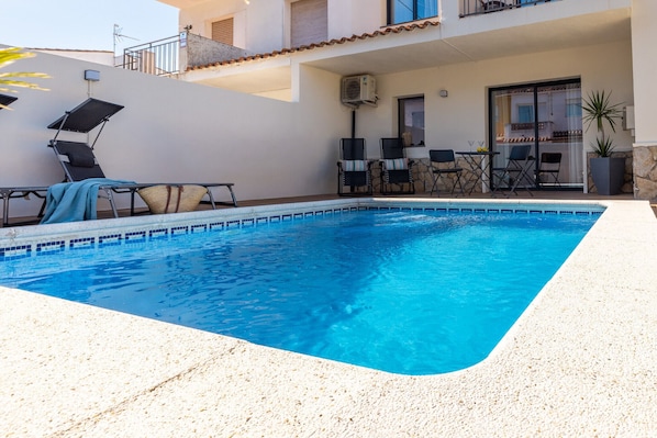 A swimming pool with lounge chairs and a table, surrounded by a building with a balcony and a potted plant. - House Montgrí, modern and comfortable, pax 8 (L'Escala)