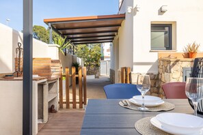 An outdoor patio with a wooden table set for dining, a stone wall, and a pergola providing shade. - House Montgrí, modern and comfortable, pax 8 (L'Escala)