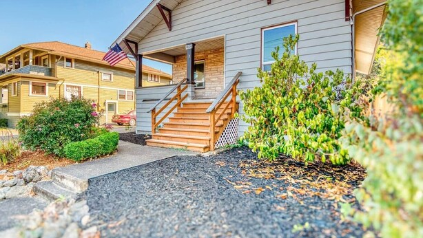 Una casa de dos pisos con un porche delantero, una escalera de madera y un pequeño jardín.