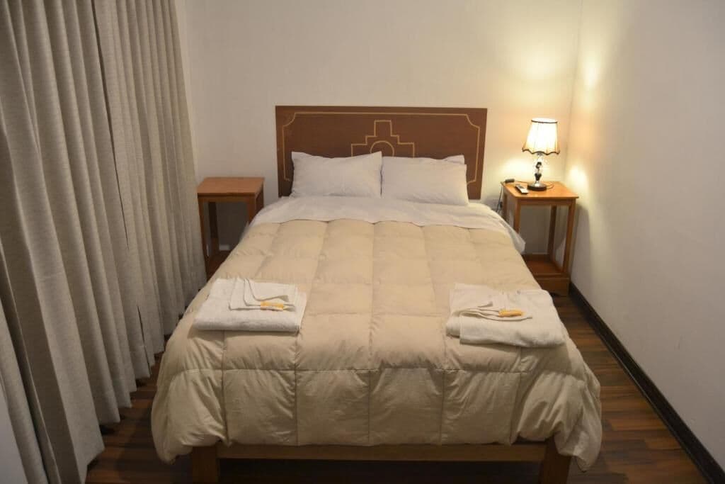 Un lit bien fait, avec une couette beige, deux oreillers et deux tables de chevet dotées de lampes.