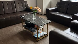 Ein Wohnzimmer mit braunem Ledersofa, einem schwarzen Couchtisch mit Zeitschriften und einem Kühlschrank.