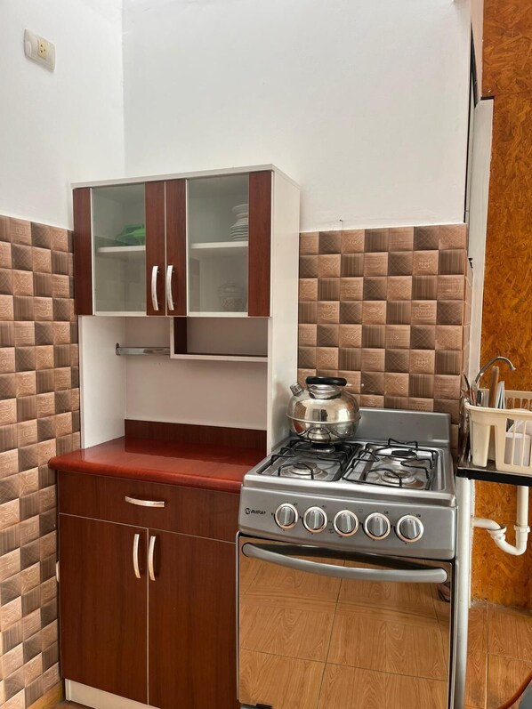 A compact kitchen with a gas stove, a cabinet with glass doors, and a tiled backsplash. - Apu Wasi (Cusco)