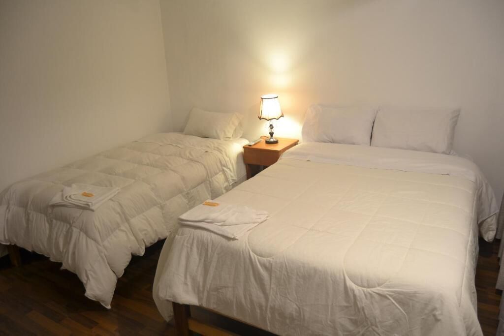 Una habitación de hotel con dos camas individuales, una mesita de noche con lámpara y suelo de madera.