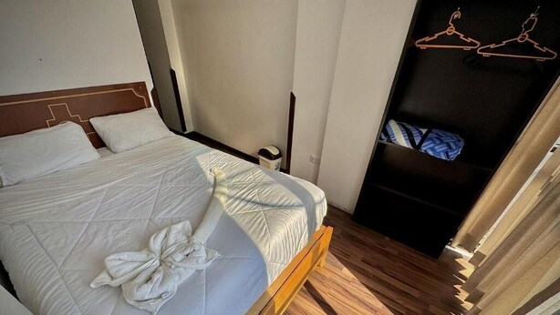 Ein Bett mit einer gesteppten Matratze und Kissen, ein Holzboden, ein Kleiderschrank mit Kleiderbügeln und eine Tür mit Vorhang.