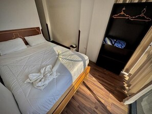 A bed with a quilted mattress and pillows, a wooden floor, a wardrobe with hangers, and a door with a curtain. - Apu Wasi (Cusco)