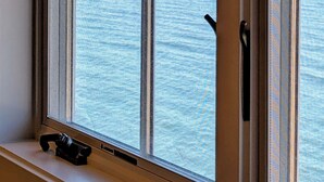 A window with a view of the sea and a sailboat.