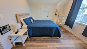 A bedroom with a bed, bedside table, lamp, and a framed picture on the wall.