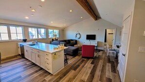 A spacious kitchen with a large island, a dining area with a red chair, a television, and a cozy seating area with a sofa and a decorative wall hanging.