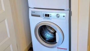 A stacked washer and dryer unit in a corner with a wooden floor.
