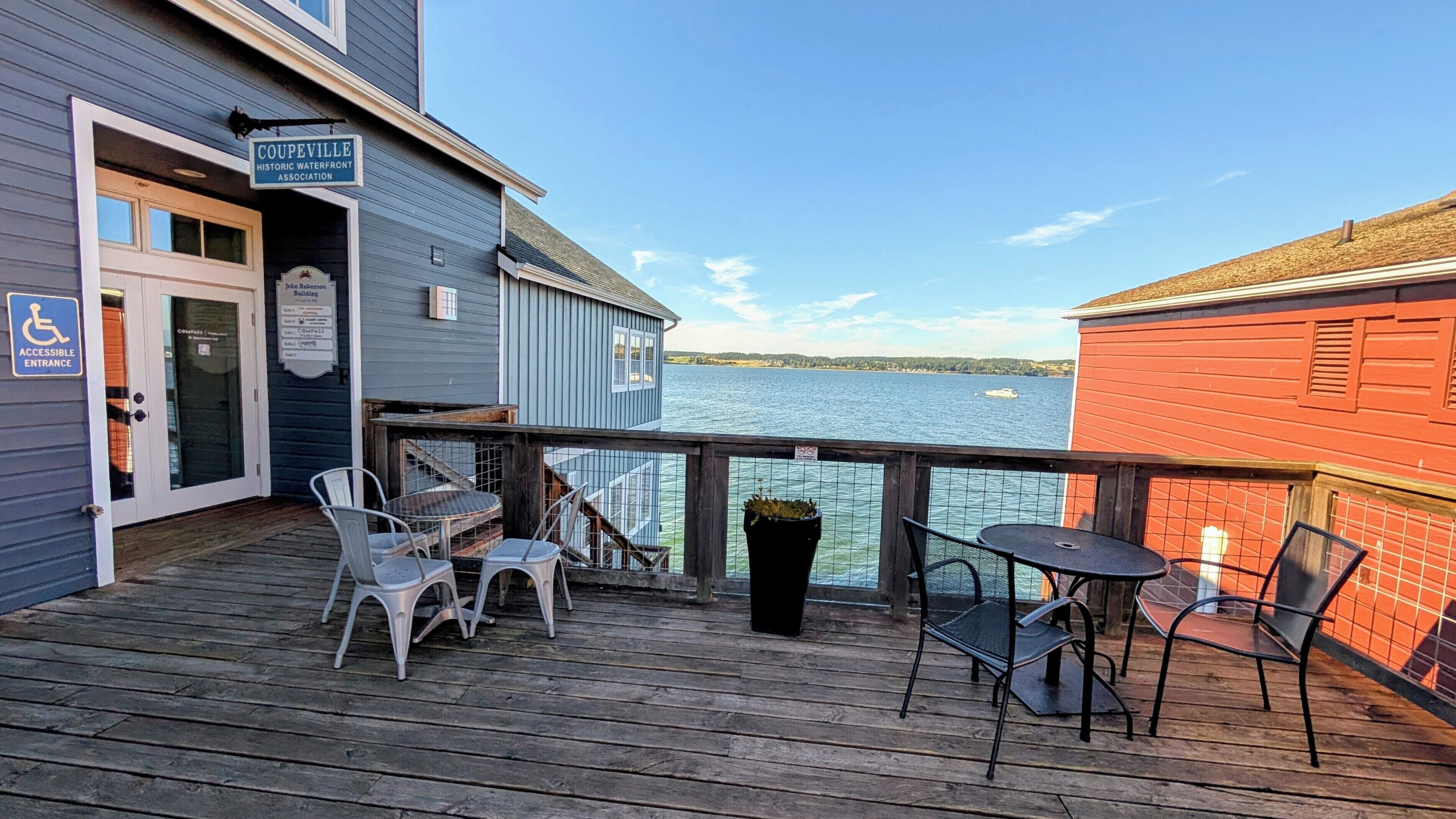 Eine Holzterrasse mit Sitzgelegenheit im Freien, ein Schild des 'Coupeville Historic Waterfront Association' und Blick auf das Wasser.