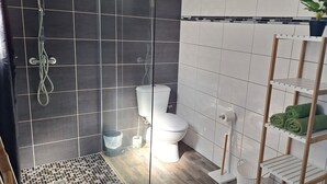 Een badkamer met douche, toilet, wastafel en planken met handdoeken.