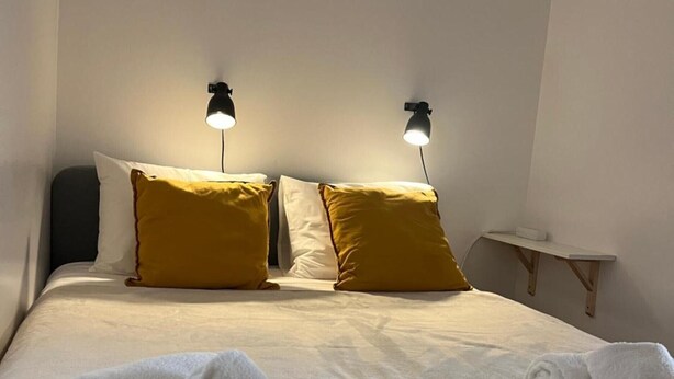 A neatly made bed with two pillows, two wall-mounted lamps, and two rolled towels. - Apartment 'O Meu Cantinho' with Wi-Fi and Air Conditioning (Elvas)