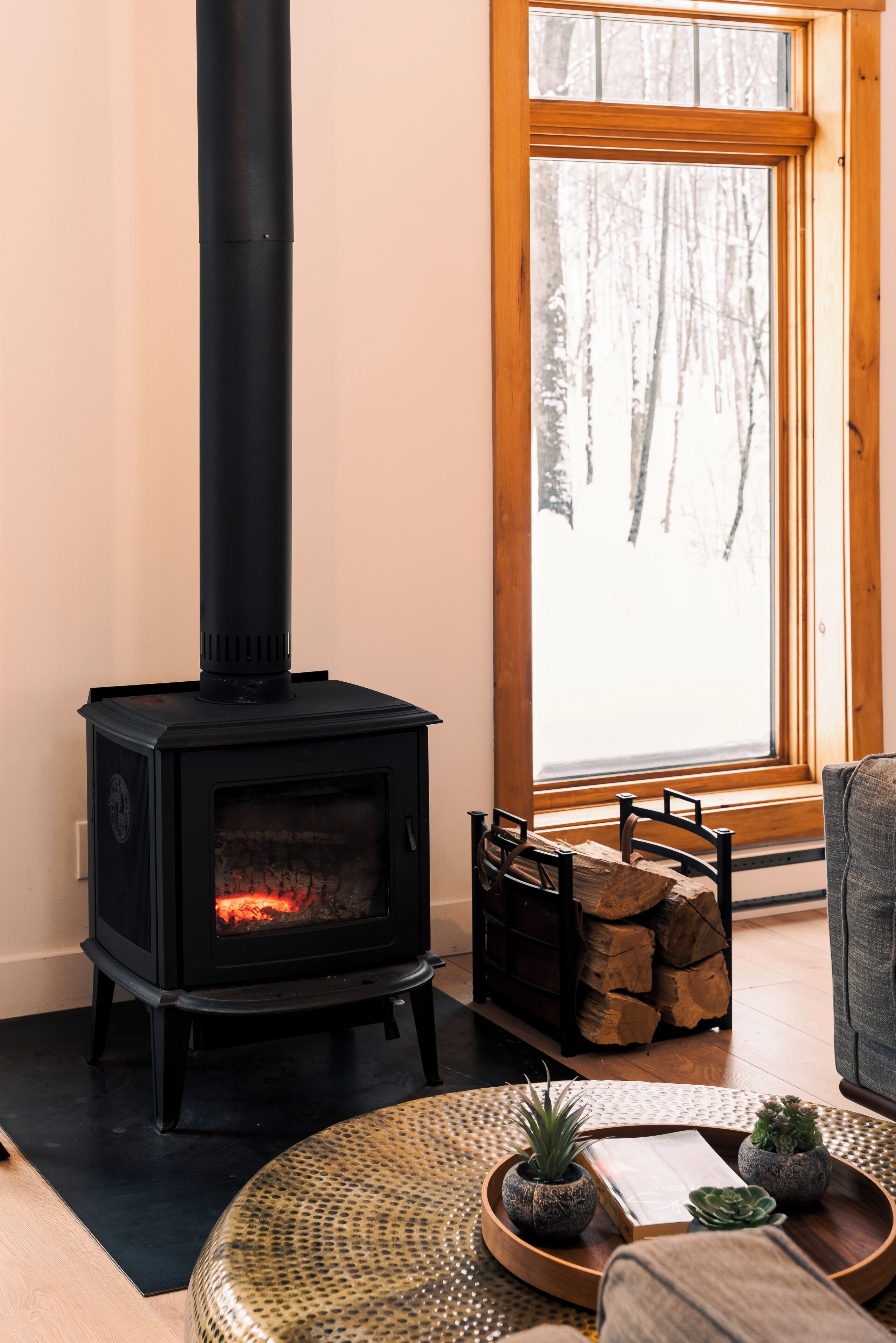 A wood-burning stove in a room with a large window, a chair, and a small table with plants.