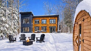Ein zweistöckiges Haus mit Holzfassade und schwarzem Anstrich, umgeben von schneebedeckten Bäumen.