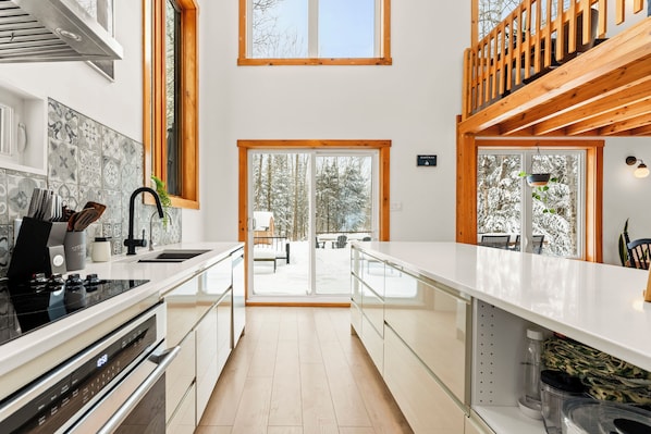 Een moderne keuken met een centraal eiland, een eethoek met uitzicht op besneeuwde bomen, en een houten bovendek.