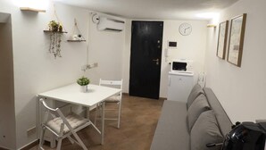 A compact living space with a dining table, chairs, a sofa, a black door, a microwave, and a small plant. - In the heart of Palermo, cozy apartment in the Historic Center. (Palermo)