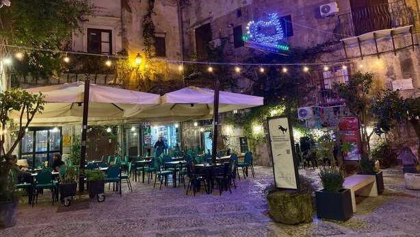 An outdoor café with tables and chairs under umbrellas, surrounded by buildings and greenery. - In the heart of Palermo, cozy apartment in the Historic Center. (Palermo)
