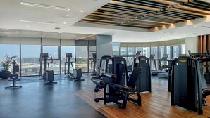 Et moderne fitnesscenter med forskellige træningsmaskiner, store vinduer med udsigt over byen og en trægulv.