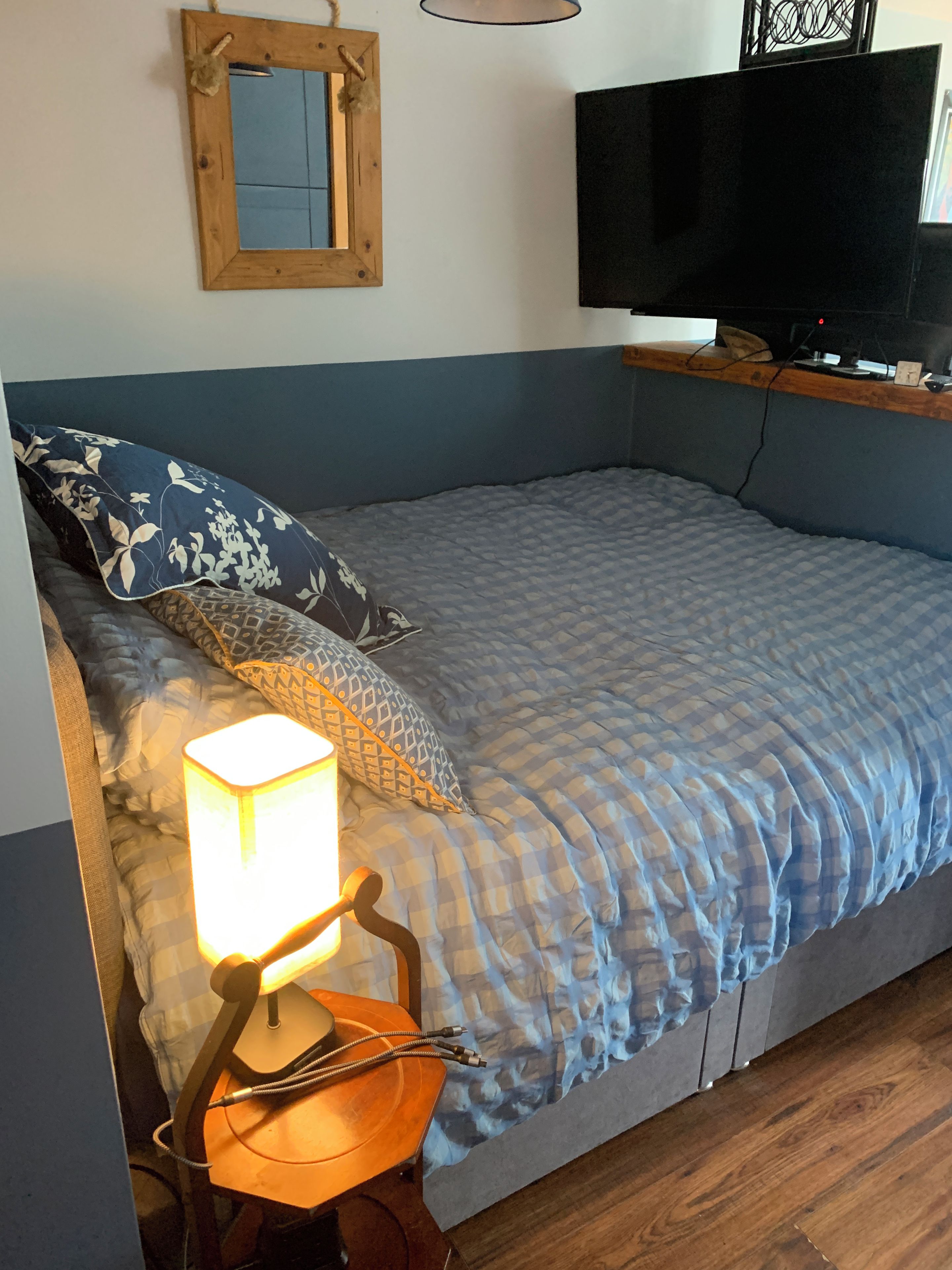 A bed with a blue and white checkered bedspread, a wooden headboard, and a bedside lamp.