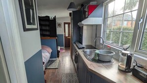 A compact kitchen with a sink, stove, and a window providing natural light. A patterned rug lines the floor, and a bed is visible in the background.