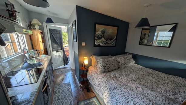 A compact bedroom with a bed, a bedside table, a lamp, and a painting on the wall.