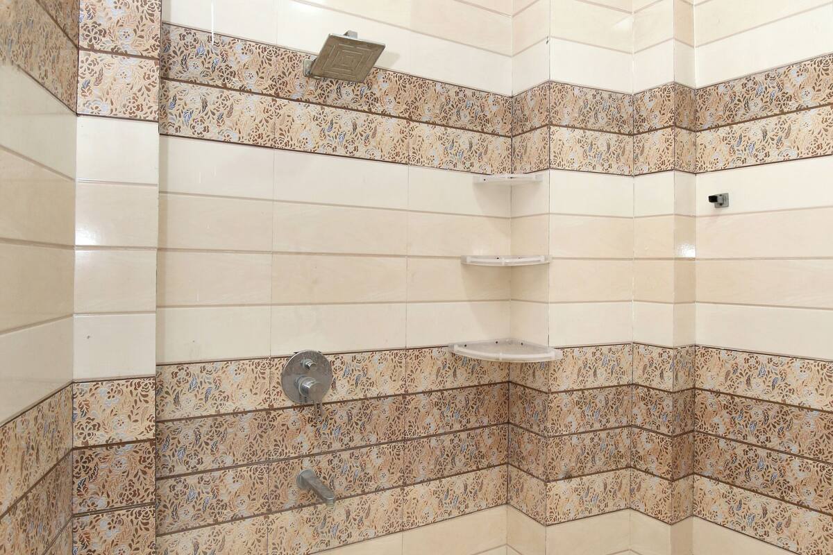 Ducha en esquina con paredes y suelo de azulejos, un cabezal de ducha y una repisa.