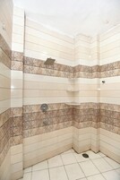Ducha en esquina con paredes y suelo de azulejos, un cabezal de ducha y una repisa.