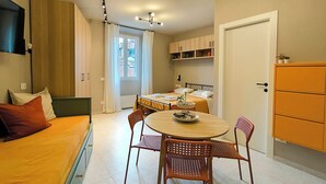 Una stanza compatta con un letto, un tavolo da pranzo con sedie, un angolo cottura e una porta.