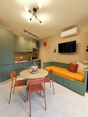 A compact living space with a kitchenette, a dining area with a round table and chairs, a sofa bed with cushions, and a mounted TV. - Drops&Dots Studio in the key area of Milan (Milano)