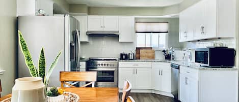 A modern kitchen with white cabinets, a wooden dining table, and a central island with a vase and plants.