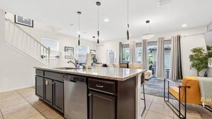 A modern kitchen with a large island, dark cabinetry, and pendant lighting. - Go!#17 WINDSOR AT WESTSIDE (Kissimmee)