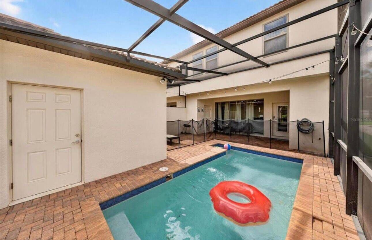 A swimming pool with a red float, a covered patio, and a door to the left.