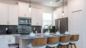 A modern kitchen with white cabinets, a stainless steel refrigerator, a built-in oven, and a bar area with stools. - Stunning 6 bedrooms Storey Lake (Kissimmee)