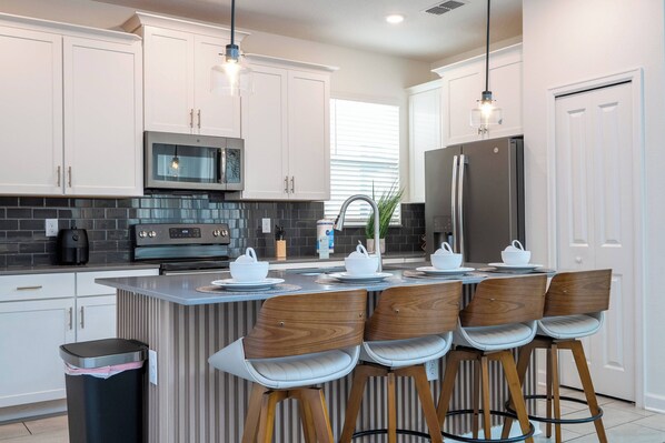 A modern kitchen with white cabinets, a stainless steel refrigerator, a built-in oven, and a bar area with stools. - Stunning 6 bedrooms Storey Lake (Kissimmee)