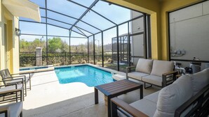 A sunlit outdoor pool area with a glass enclosure, a sofa, and a table. - Stunning 6 bedrooms Storey Lake (Kissimmee)