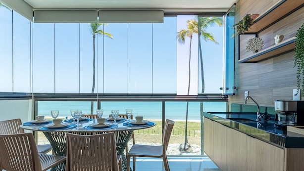 A dining area with a view of the beach, a kitchen with a sink, and wooden cabinets.