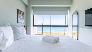 A hotel room with a large bed, a view of the beach, and a TV on the wall.