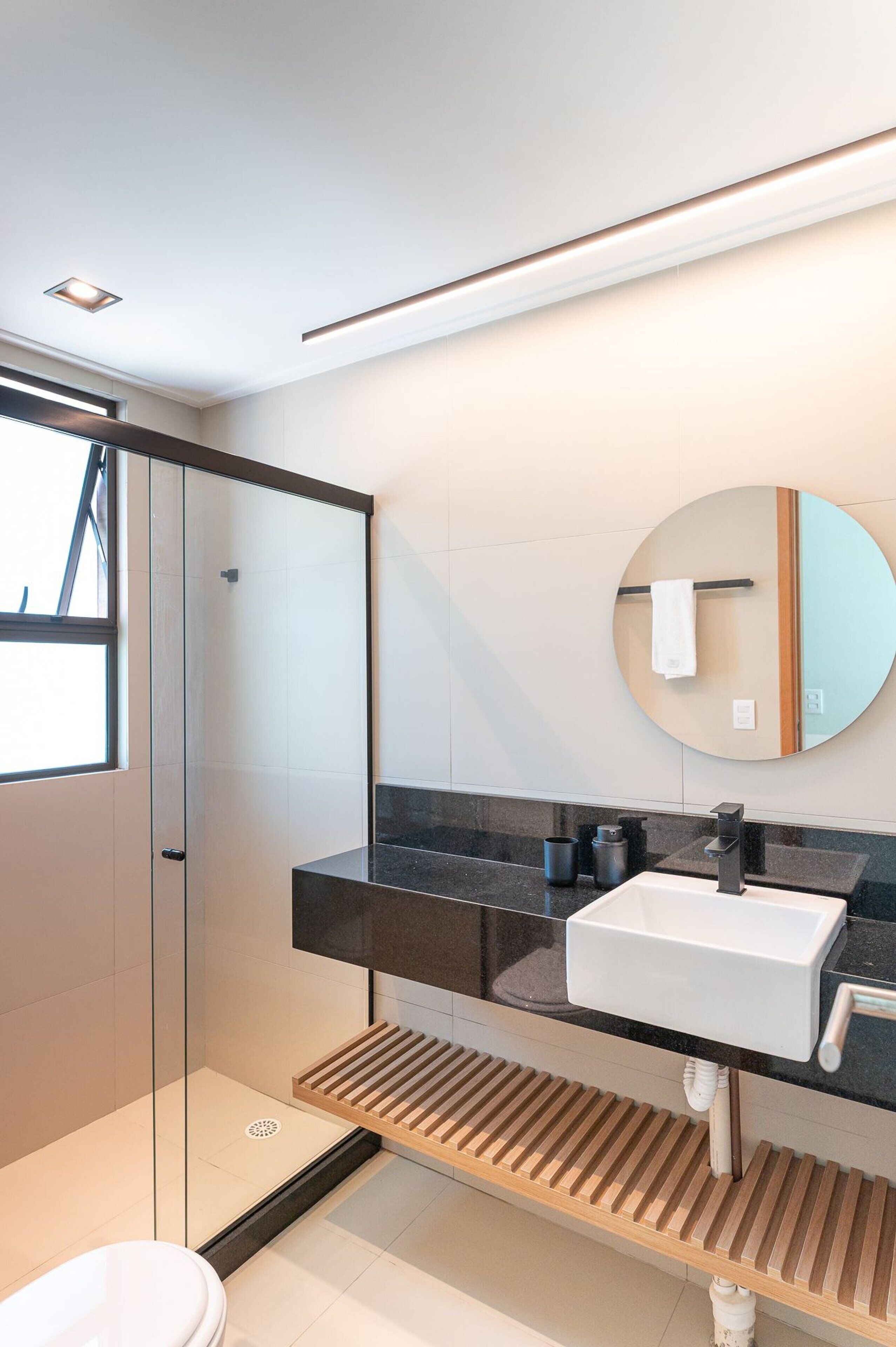 A modern bathroom with a glass shower enclosure, a white sink, and a round mirror.