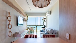 A modern living room with a wooden dining table, a sofa, and a TV mounted on the wall.
