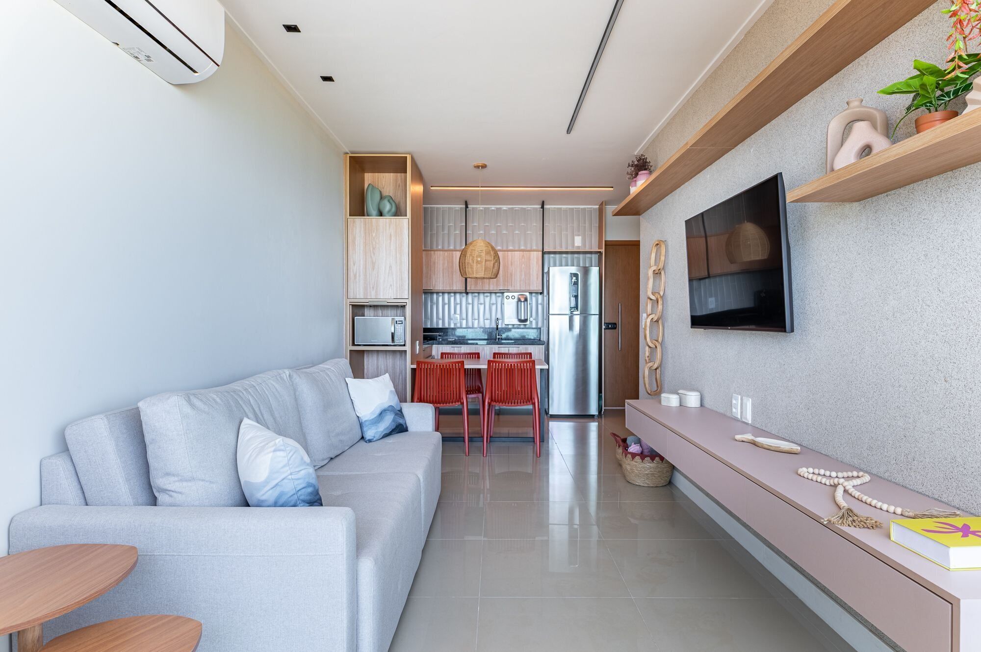 A modern living room with a grey sofa, a kitchen area with a fridge and microwave, and a dining table with chairs.