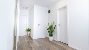 A hallway with wooden flooring, white walls, and two doors. There are two potted plants, one on each side of the hallway. - Two-bedroom family rooms apartment Casa Del Mar 4 with private balcony (Stara Novalja)