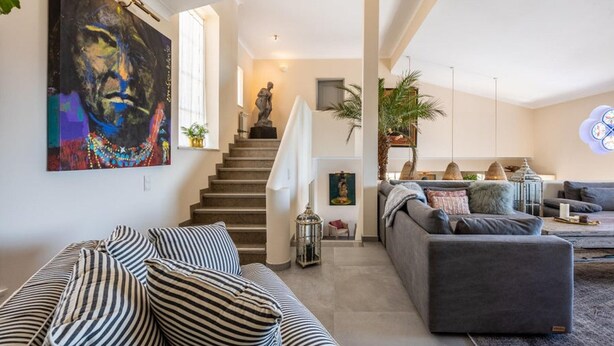 Una sala de estar moderna con una escalera, un sofá, un diván gris y un cuadro en la pared.
