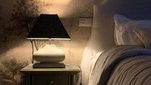 Un dormitorio con cama, mesita de noche con lámpara y pared decorada con un mural de un árbol.