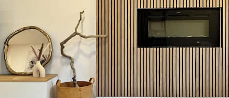 A modern living room with a wooden slatted wall, a black TV mounted on it, a white console table with a gold-framed mirror, and a brown woven basket with a branch.
