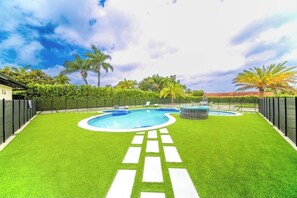A swimming pool with a clear blue water feature, surrounded by artificial grass and palm trees.